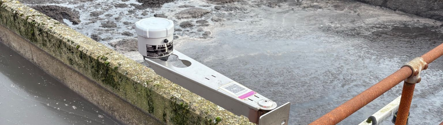A VEGAPULS Air series radar level sensor on a mounting bracket above the sludge retention basin.
