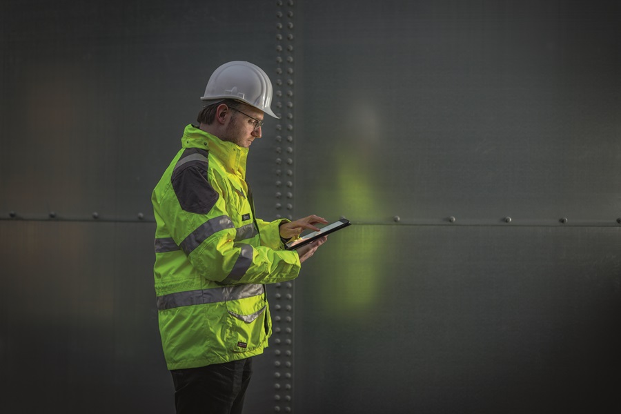 Ein Mitarbeiter in Schutzkleidung prüft auf seinem Tablet die Füllstände, die vom Radarsensor übermittelt werden.